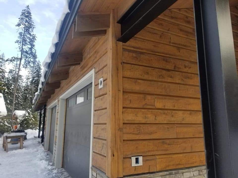 A wooden house with a gray garage door and a snowy roof