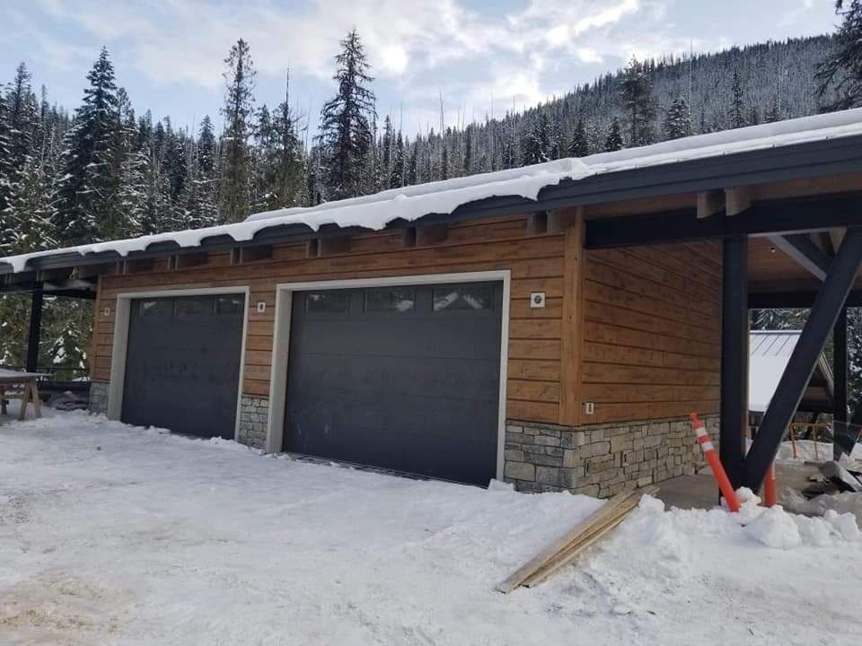 A garage with two black garage doors is covered in snow.