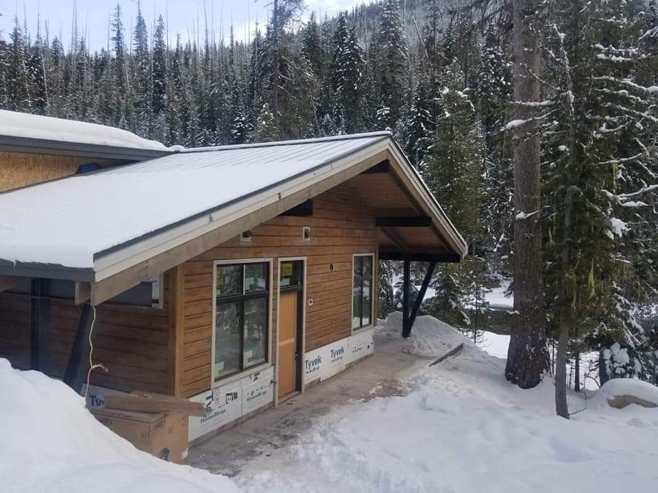A snow-covered cabin with a metal roof nestled in a snowy forest.