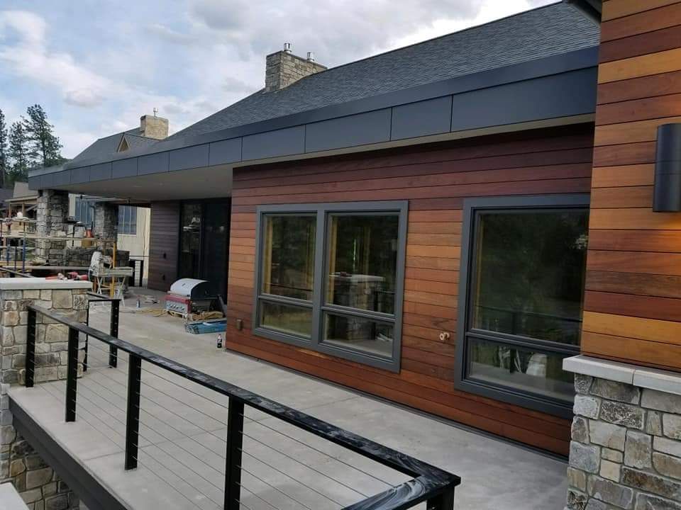 Exterior of a modern house with wood siding, large windows, and a balcony with black railing.