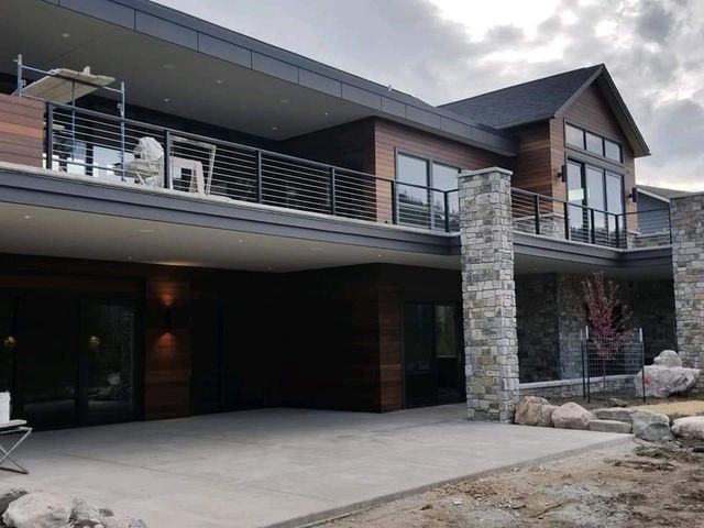 Modern home exterior with dark wood siding, balcony, and stone pillars.