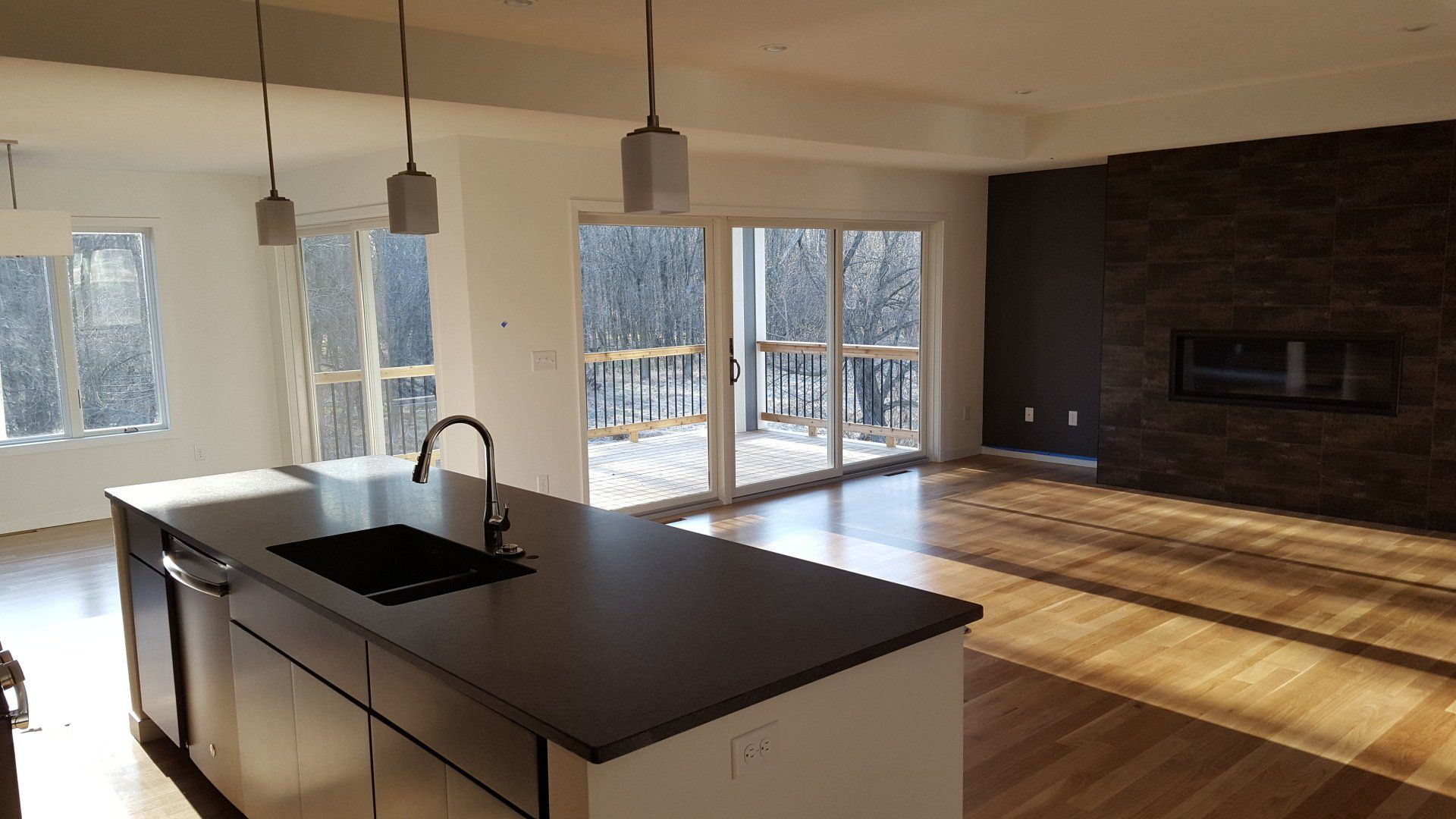 Modern open-concept kitchen and living room with island, fireplace, sliding doors, and outdoor view.