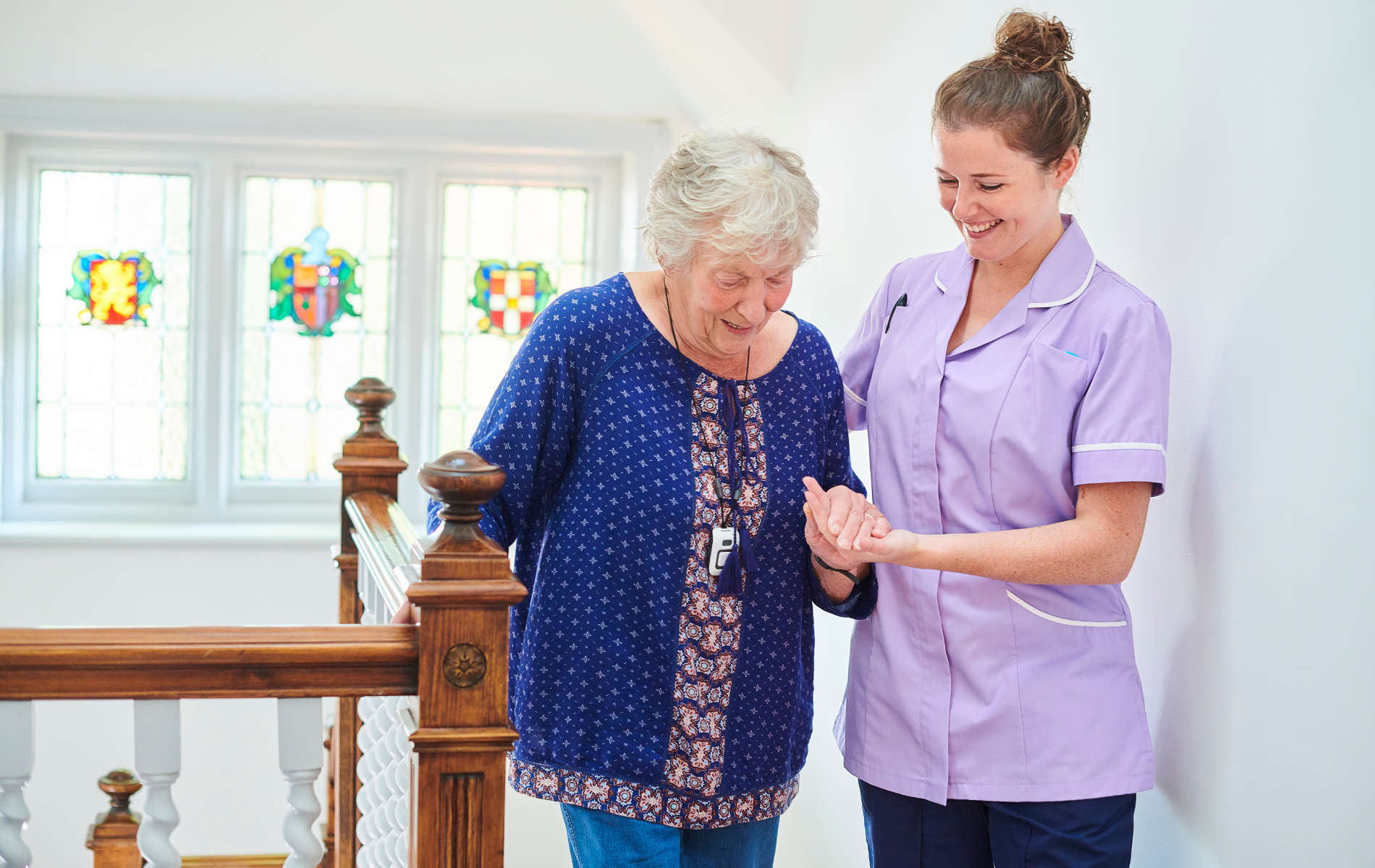 A nurse is helping an elderly woman walk down a staircase.
