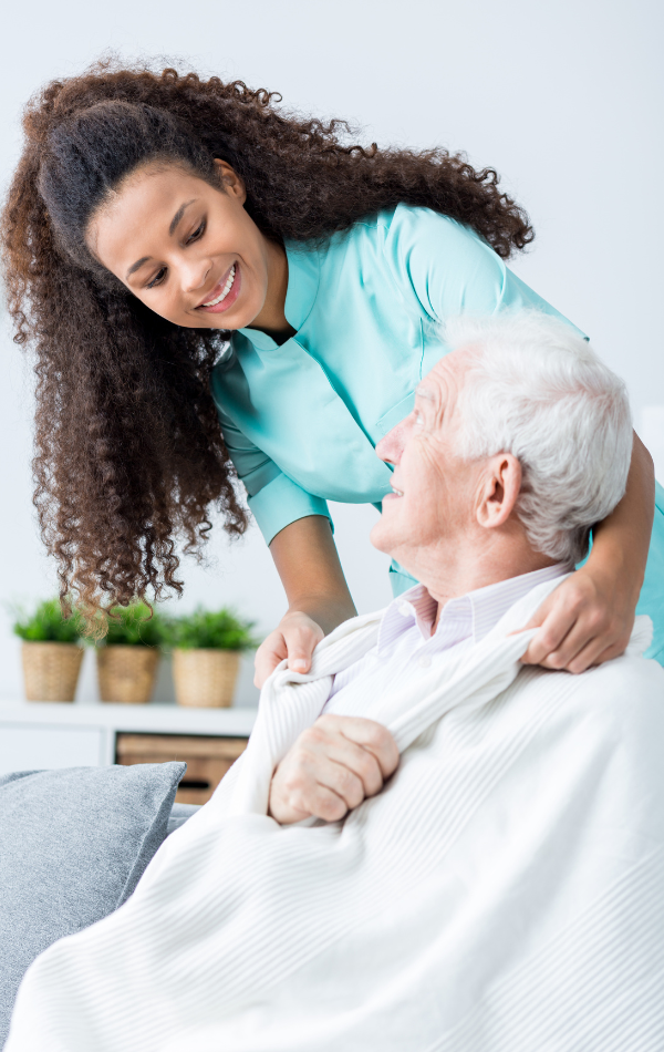 A nurse is putting a blanket on an elderly man in a wheelchair.