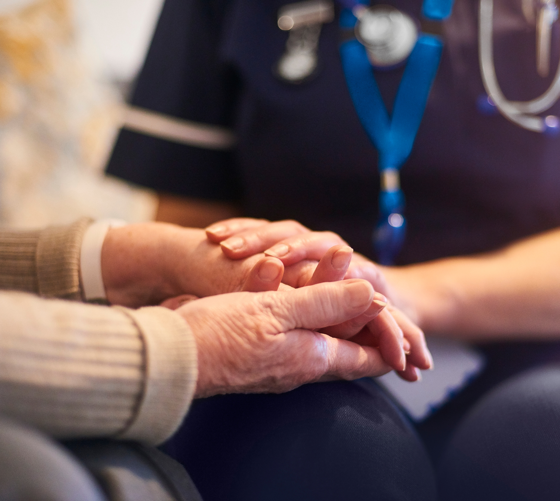 A nurse is holding the hands of an elderly woman.