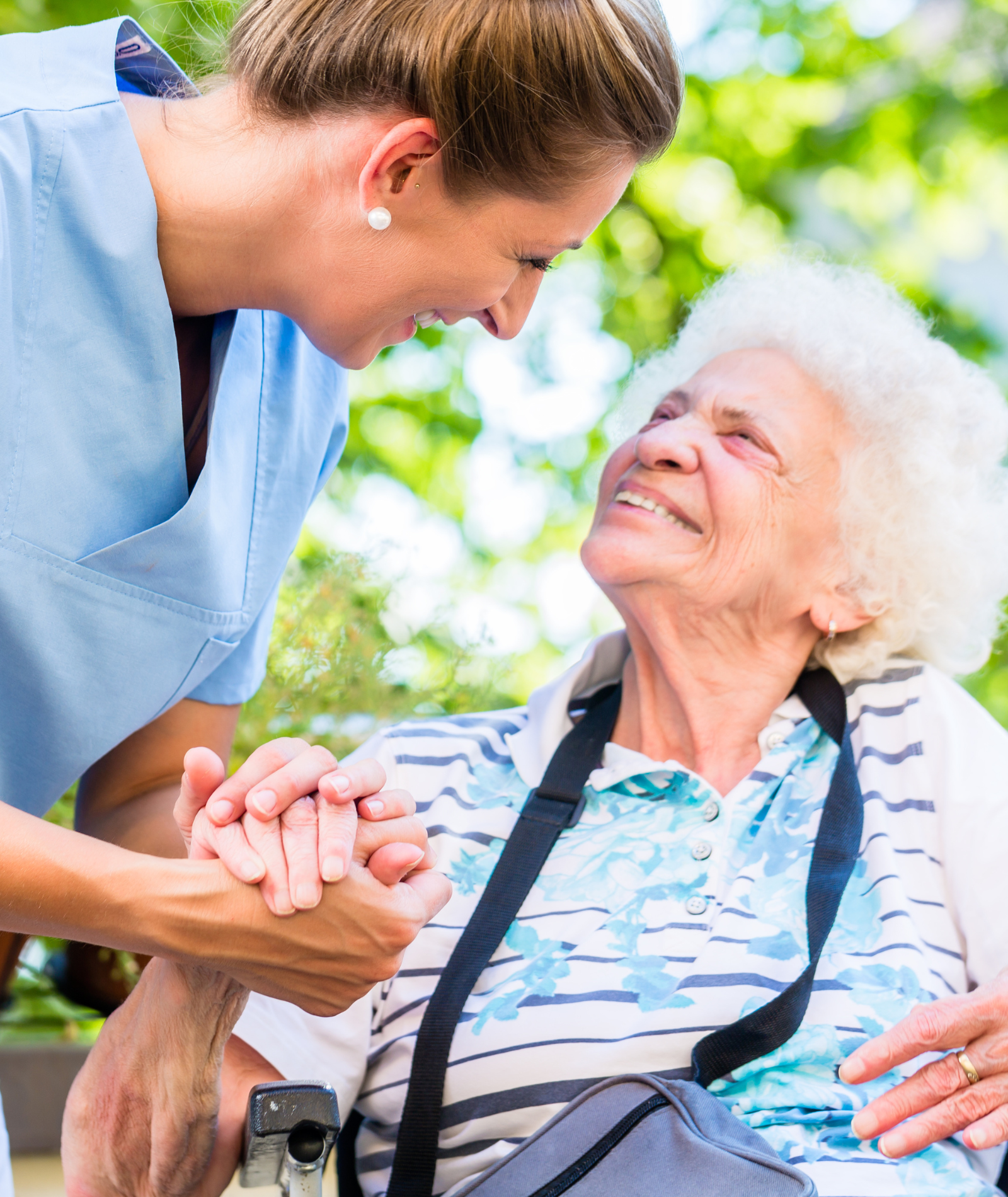A nurse is holding the hand of an elderly woman in a wheelchair.