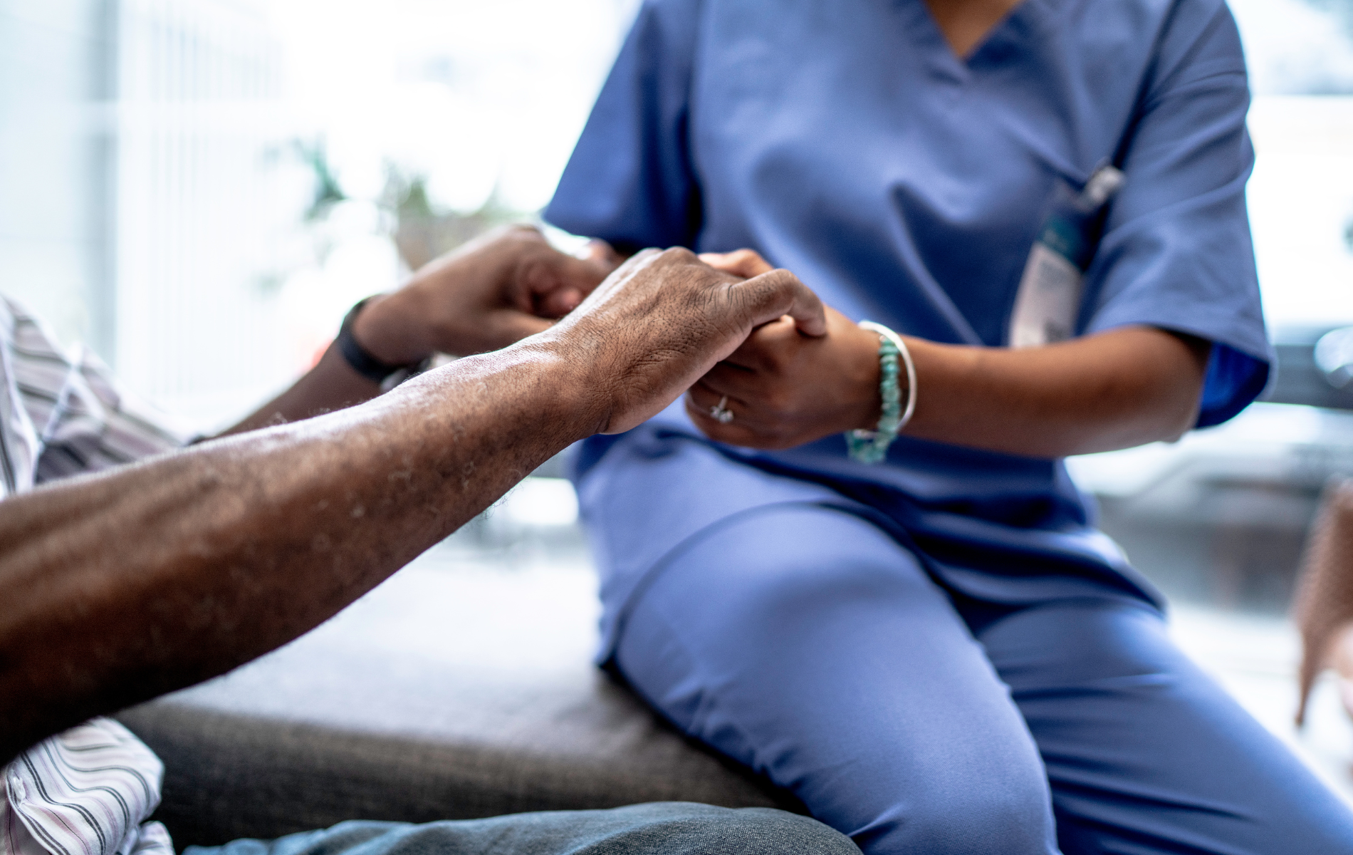 A nurse is holding the hand of an elderly man.
