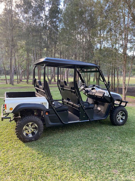 A White Golf Cart is Parked in a Grassy Field — Lift It Equipment in Sydney, NSW