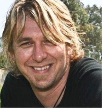 A Man With Long Blonde Hair Is Smiling — Lift It Equipment in Summerland Point, NSW