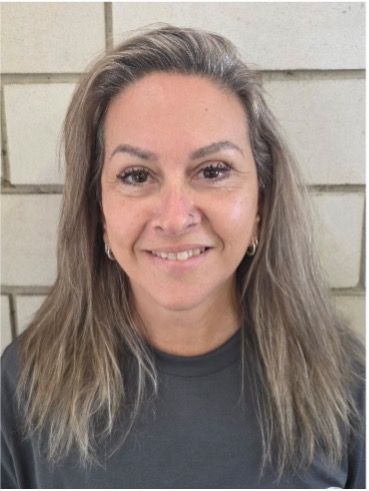 Smiling woman with long gray hair in a dark shirt standing against a light wall