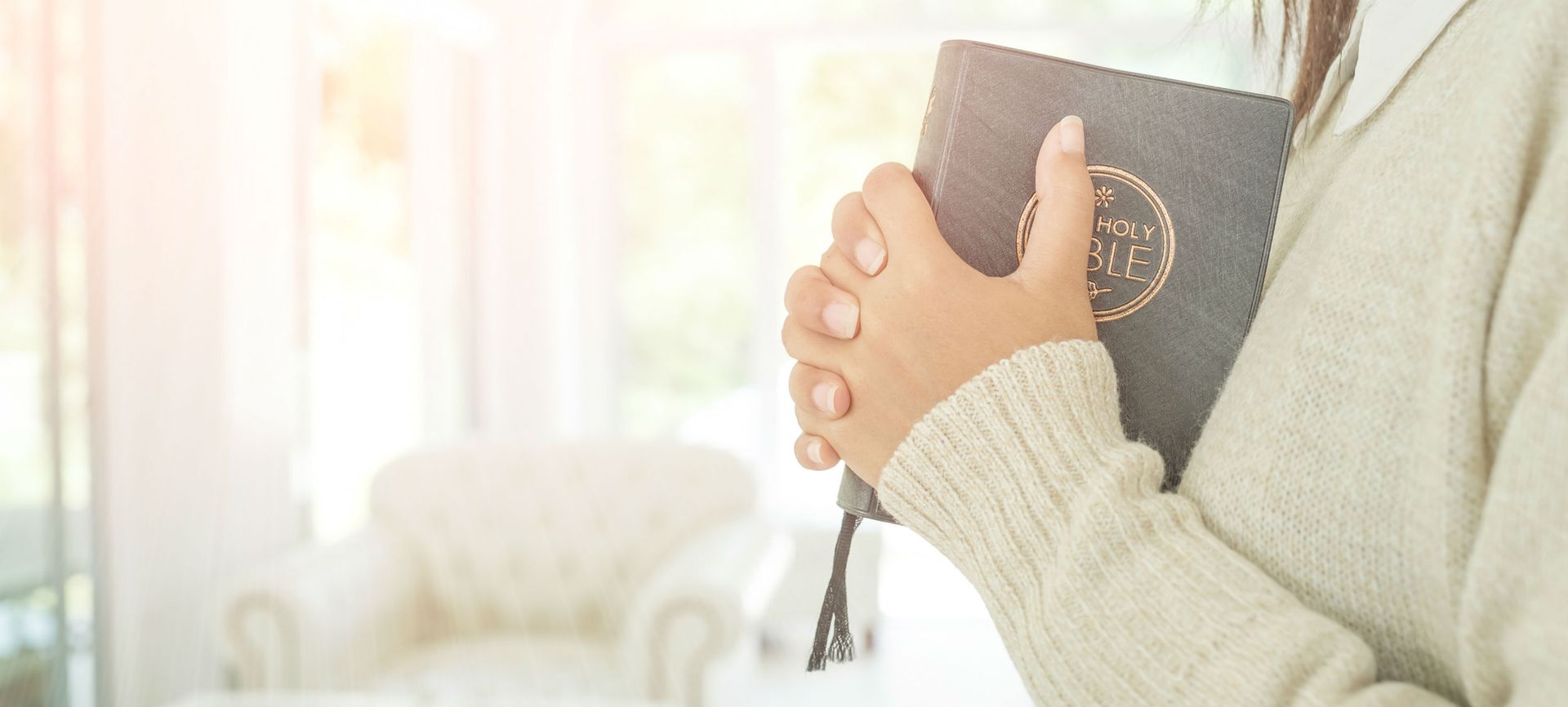 A woman is praying while holding a bible in her hands.