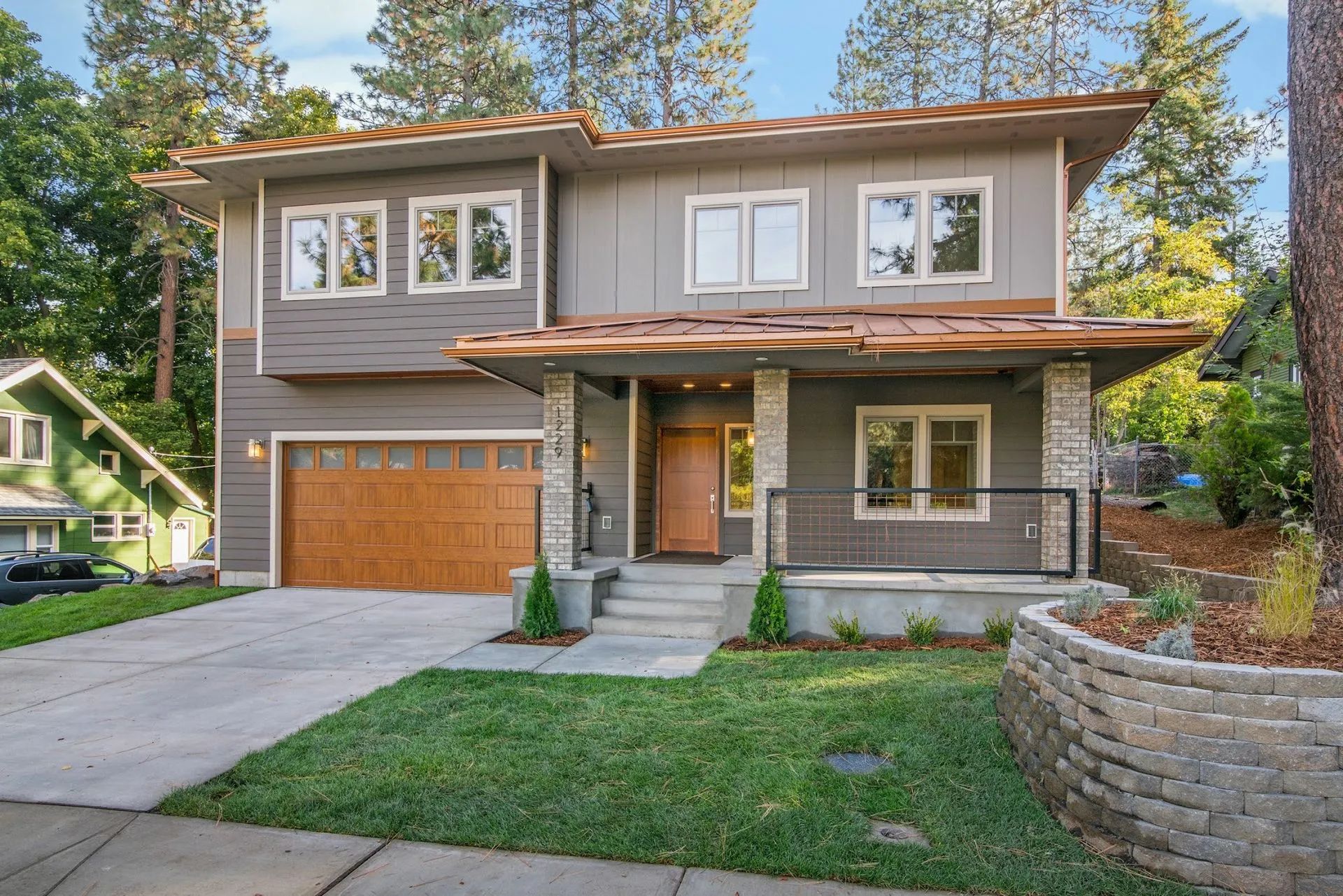 Two-story gray house with wooden garage door and porch, front yard with grass.