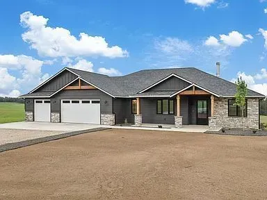 A large house with two garages is sitting on top of a dirt field.