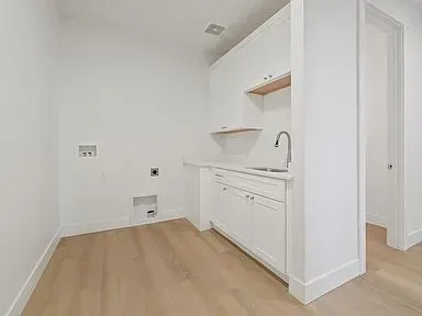 A laundry room with white cabinets and a sink.