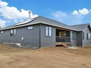 A large gray house with a lot of windows is sitting on top of a dirt hill.
