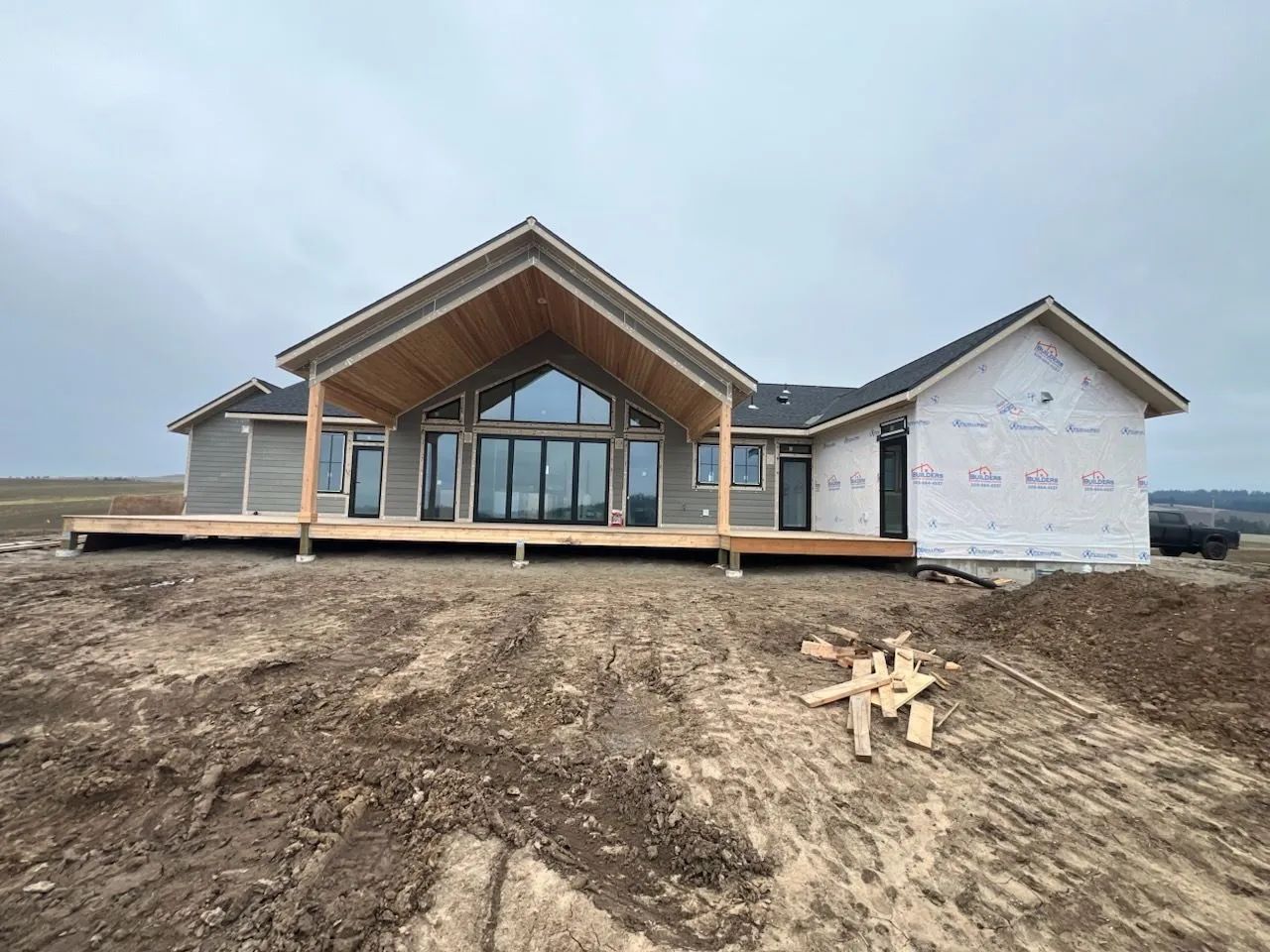 A house under construction on a dirt mound with a large deck and exposed wood framing.