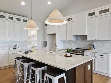 A kitchen with white cabinets and a large island with stools.