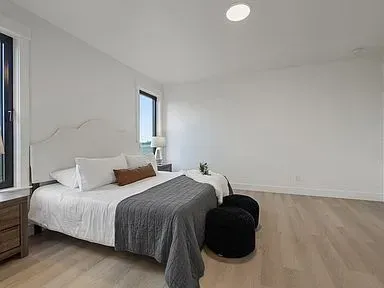 A bedroom with a bed , two ottomans , two nightstands and a window.