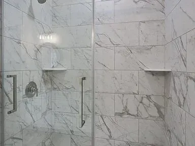 A shower stall with marble tiles and a glass door.