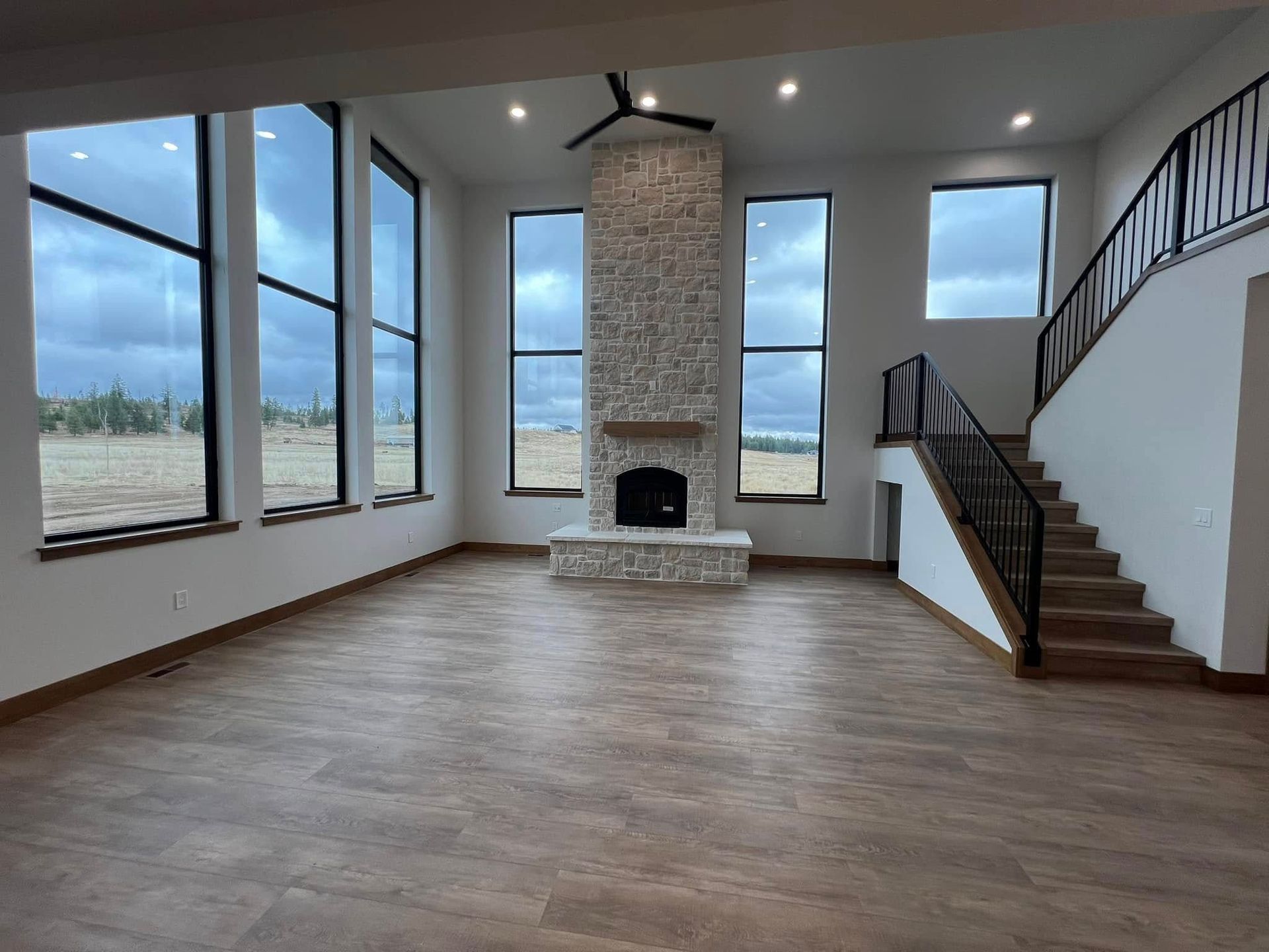 Large, modern house with stone facade, dark roof, and manicured lawn. Mountains in the background.