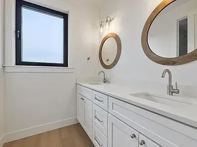 A bathroom with two sinks , two mirrors and a window.
