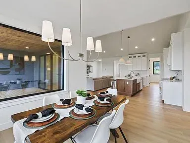 A dining room with a wooden table and white chairs and a large window.