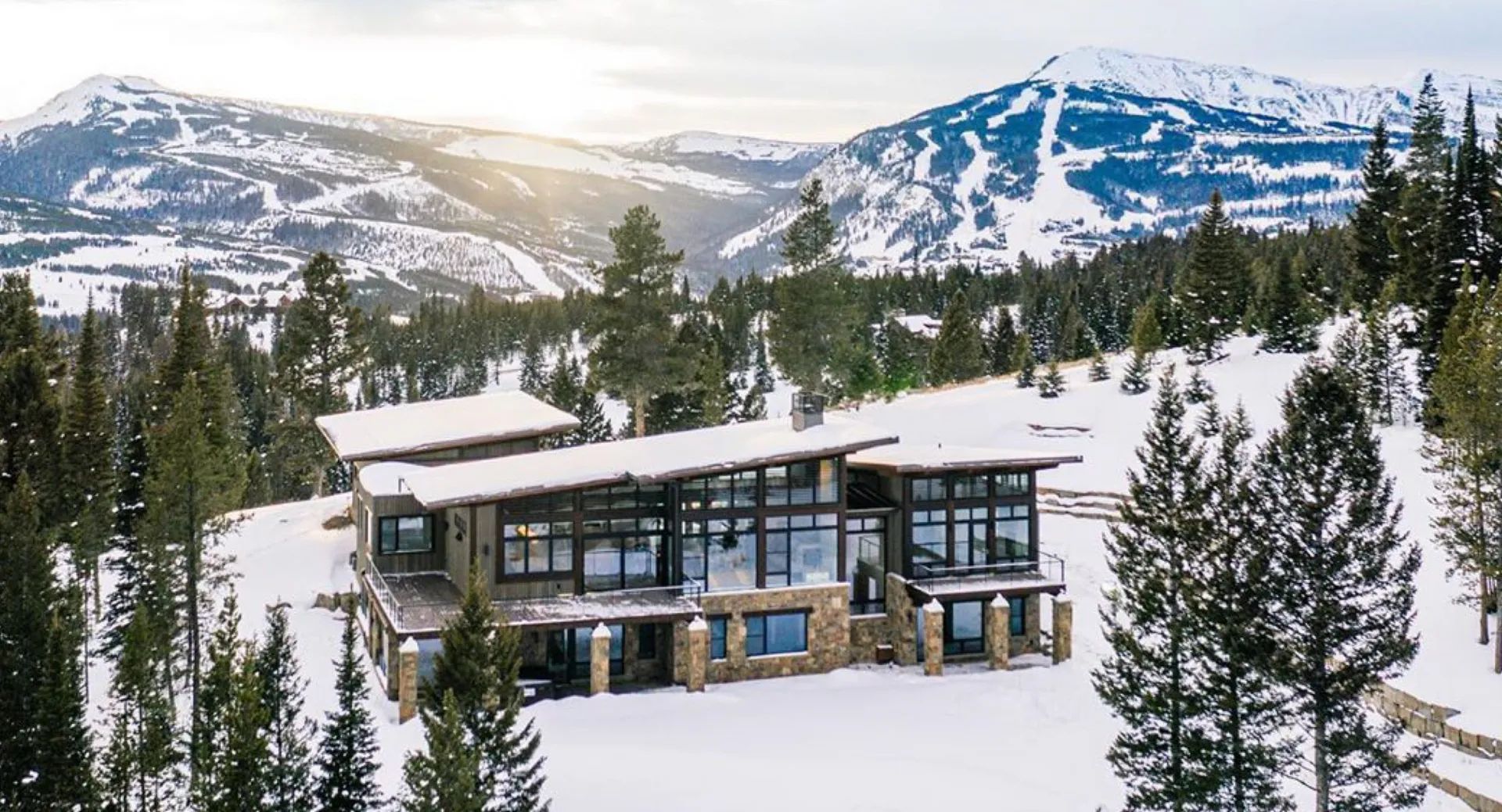 Mountain home in snow; large windows with snowy peaks in background.