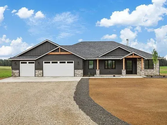 A large house with two garage doors and a gravel driveway.