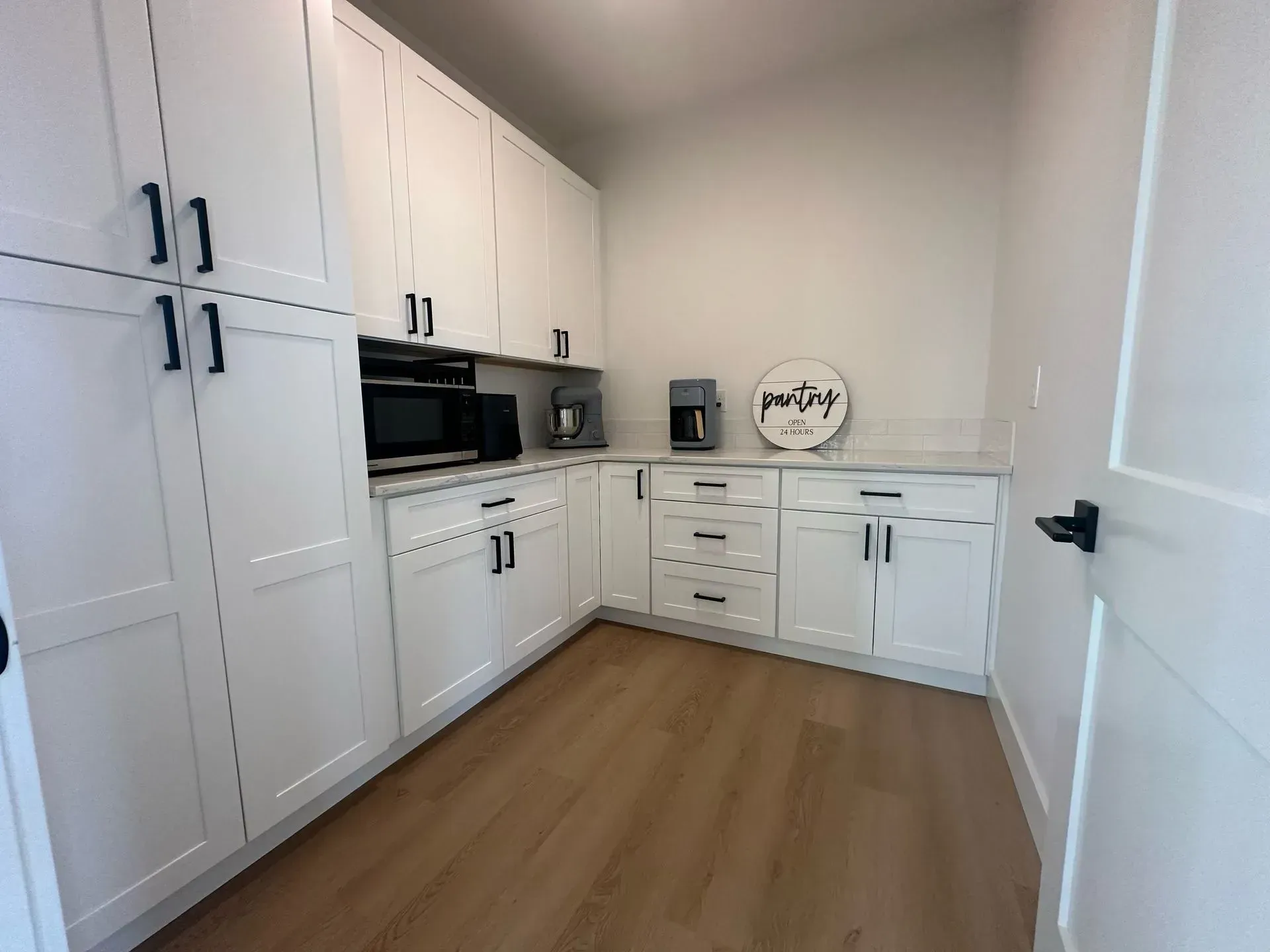 A kitchen with white cabinets , wooden floors , a microwave and a coffee maker.