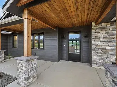 The front porch of a house with a wooden ceiling and stone pillars.