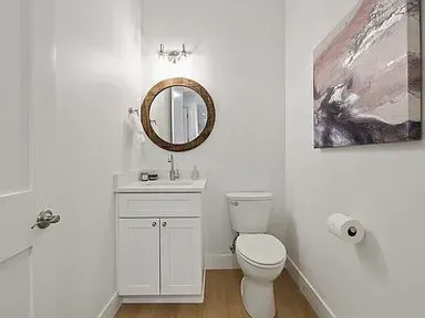 A bathroom with a toilet , sink , mirror and painting on the wall.