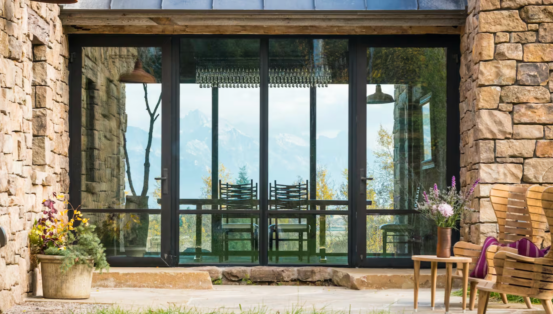 Dining room with long table, red chairs, art, wooden walls, and large window overlooking a wet outdoor space.