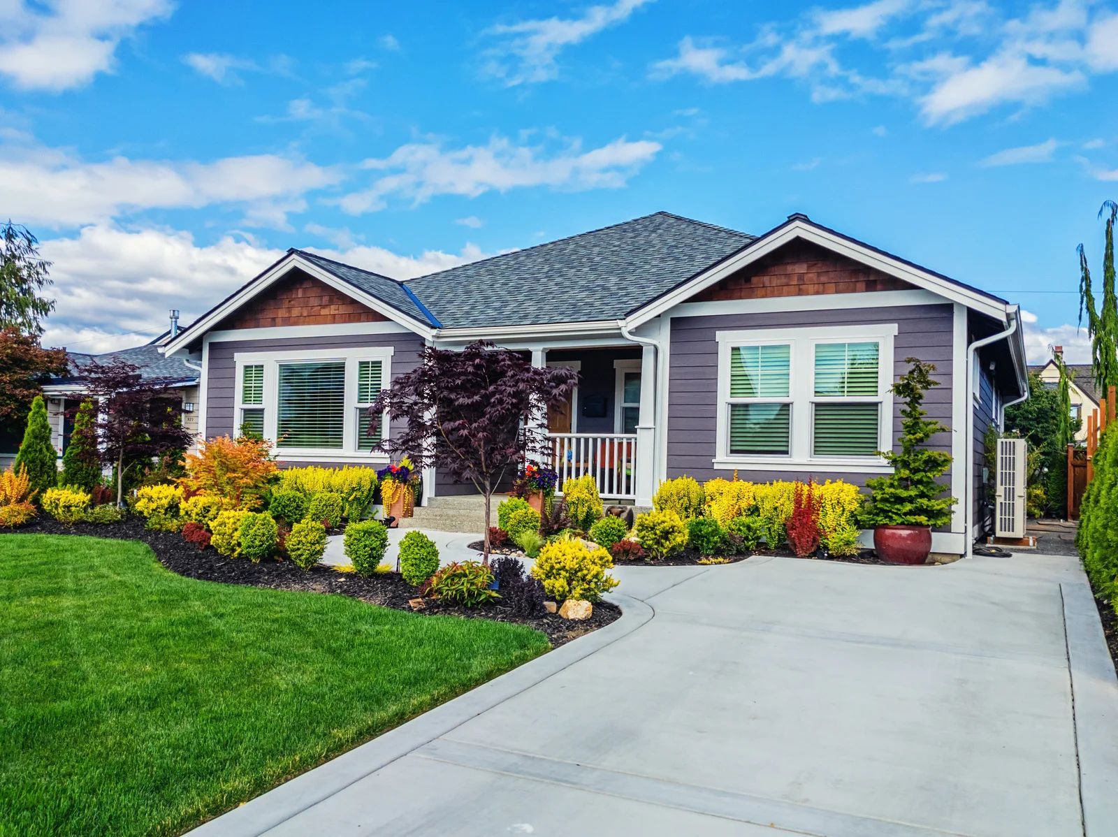 Purple bungalow with white trim, a concrete driveway, and a landscaped front yard on a sunny day.
