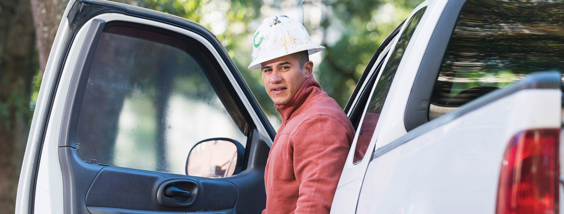 Industrial driver of a 4 door white pickup with a hard hat.