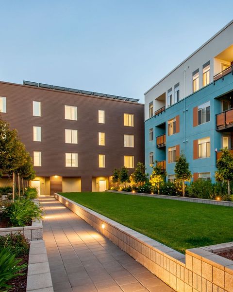 Courtyard with brown and blue apartment buildings, green lawn, and a lit pathway.