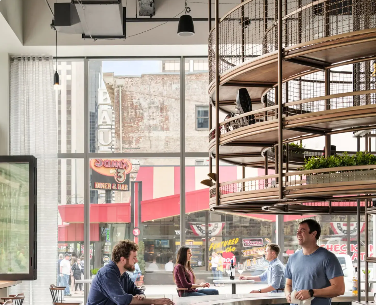 Restaurant interior with spiral shelving, large windows overlooking street with storefronts, and people dining.