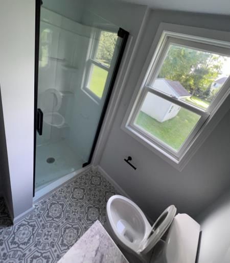 Bathroom with shower, toilet, and window, featuring patterned floor tiles and black accents.