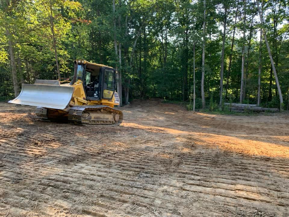 Yellow bulldozer parked on a cleared, muddy construction site near a dense forest.