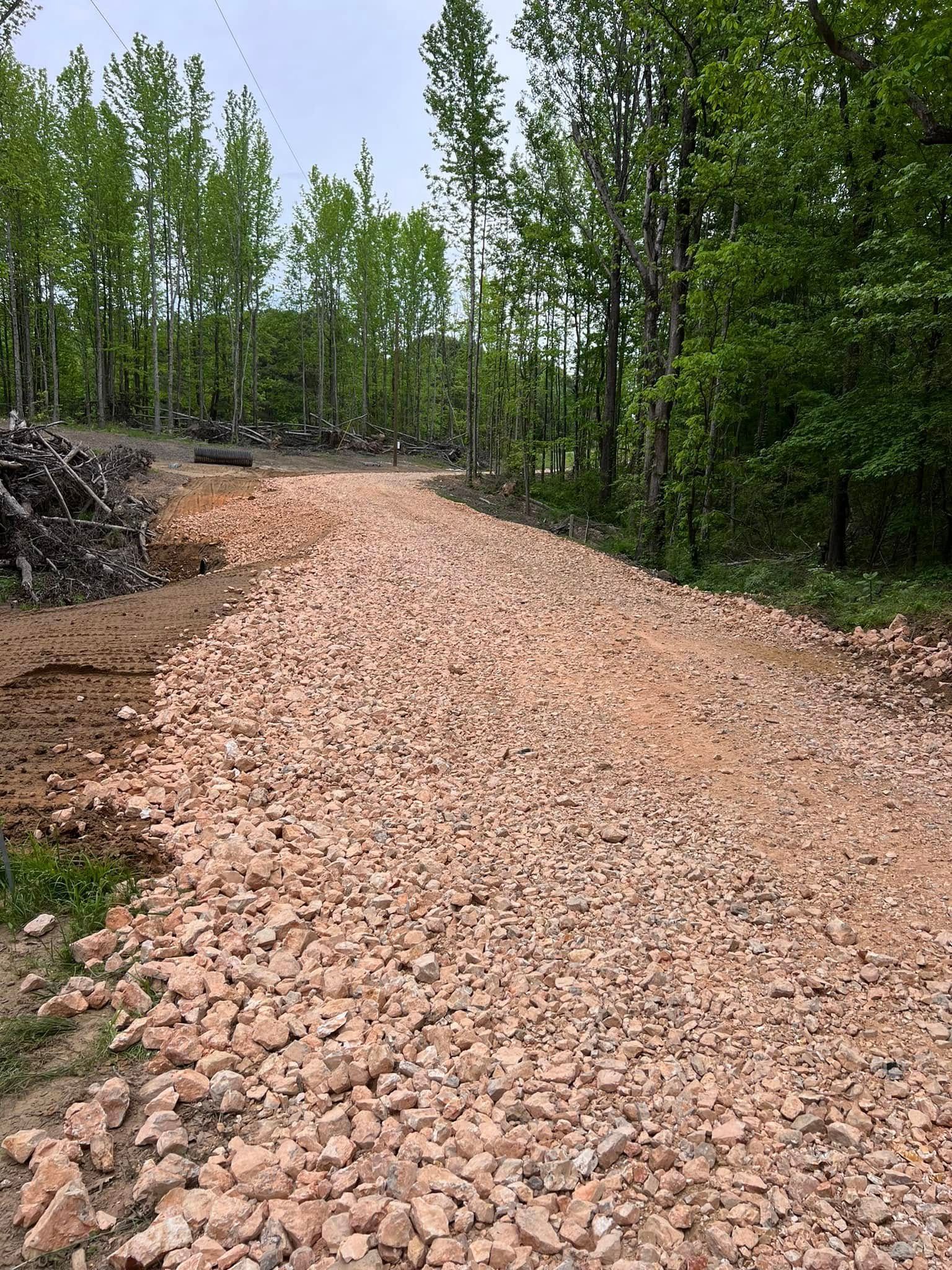 A wide path covered in light-colored gravel leading into a forest with green trees under a cloudy sky.