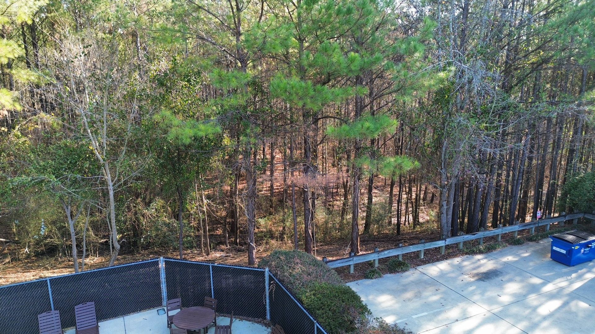 An elevated view of a patio with chairs next to a parking lot and a dense forest background.