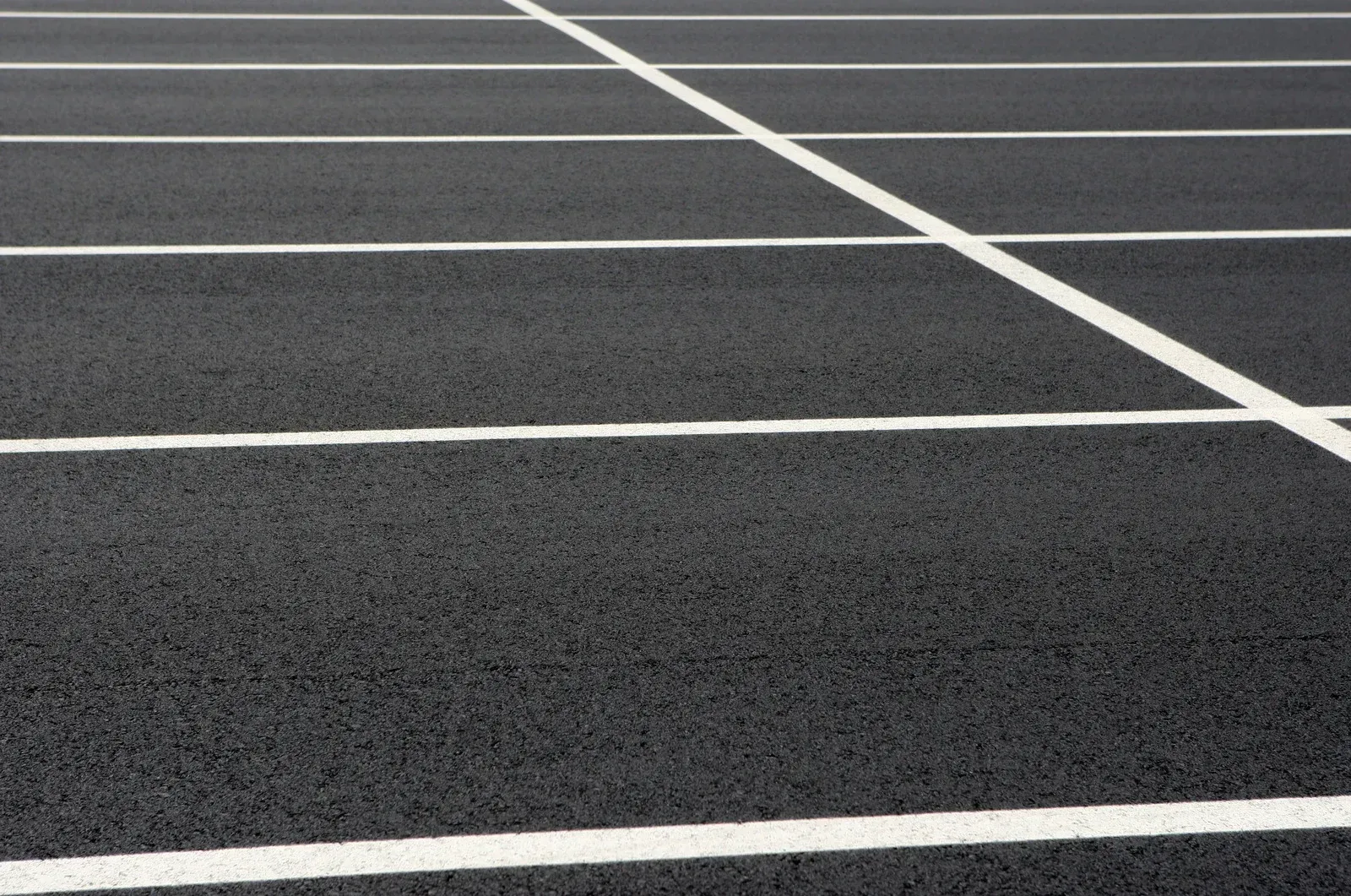 A view of an empty parking lot with white painted lines dividing empty spaces against dark asphalt.