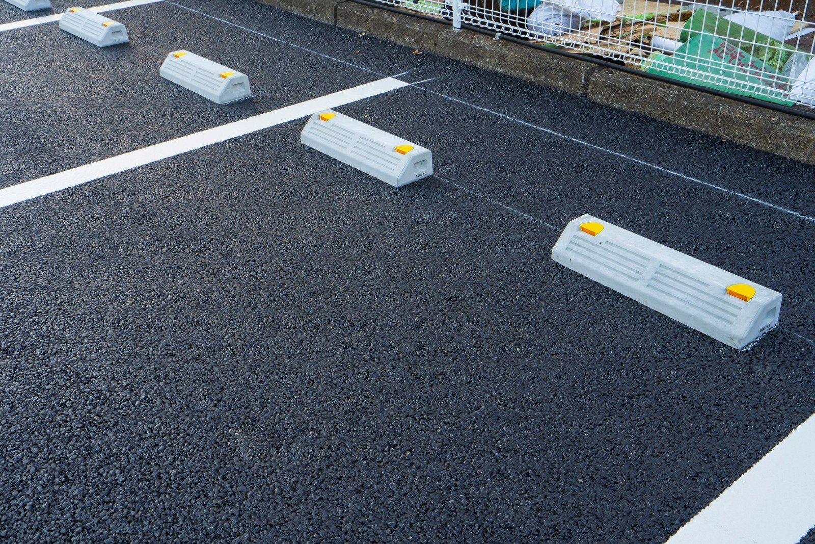 Several concrete parking bumpers with yellow reflectors sit on a freshly paved black asphalt parking lot.