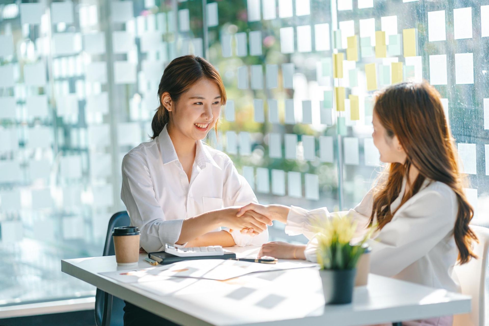 Two women are shaking hands while sitting at a table.