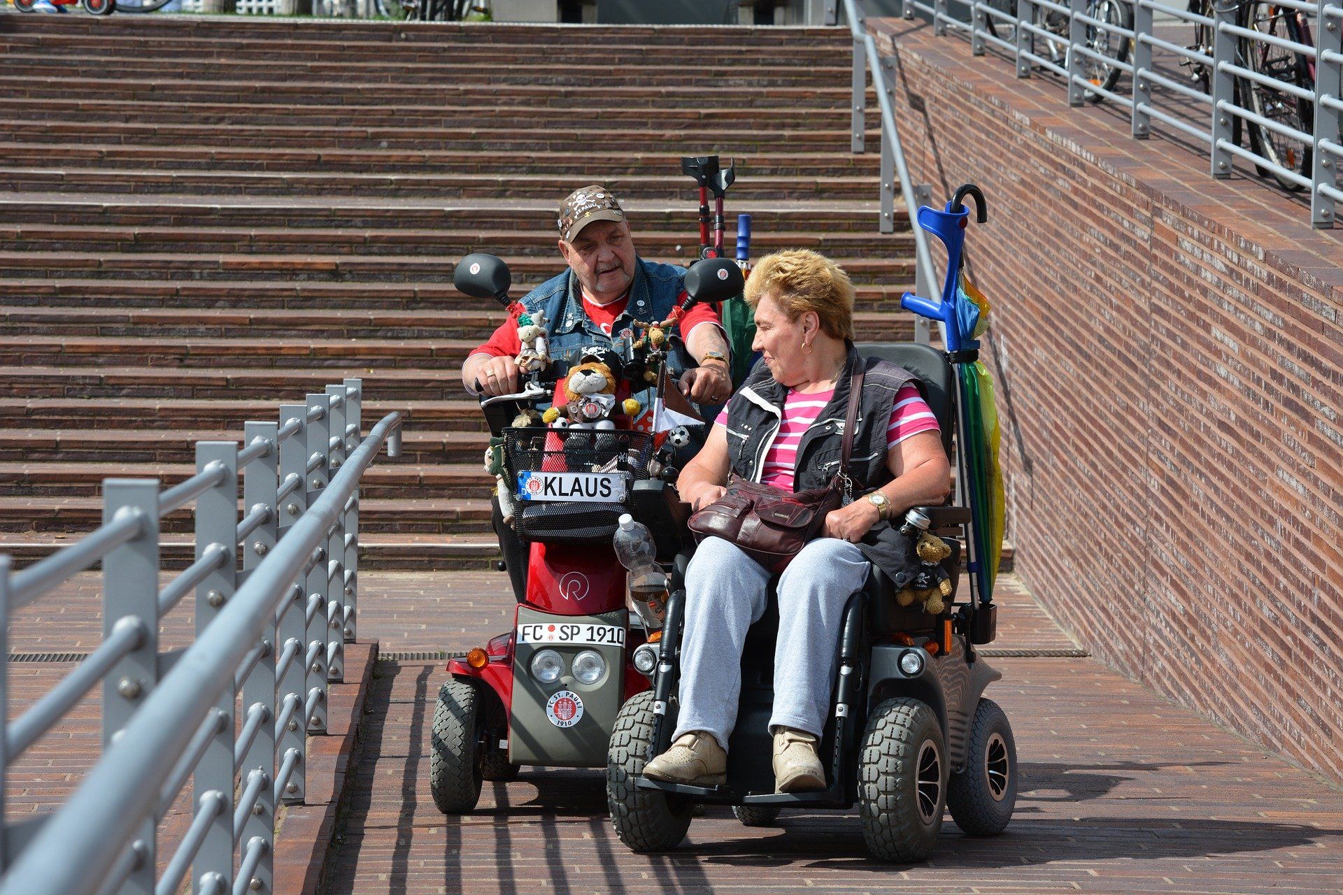 A middle-age man and woman sit in their motorized wheelchairs that are adorned with flair.
