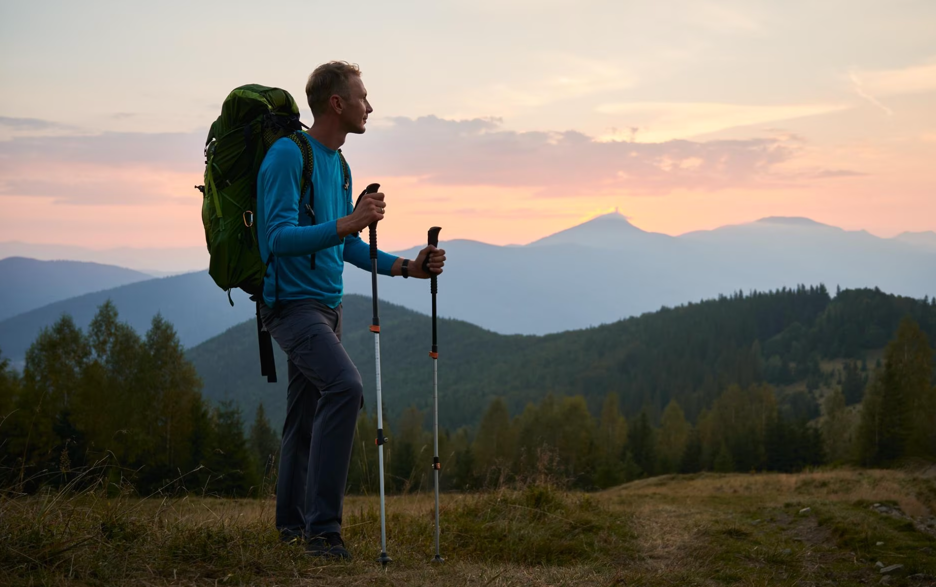 A man with a backpack and hiking poles is standing on top of a hill.