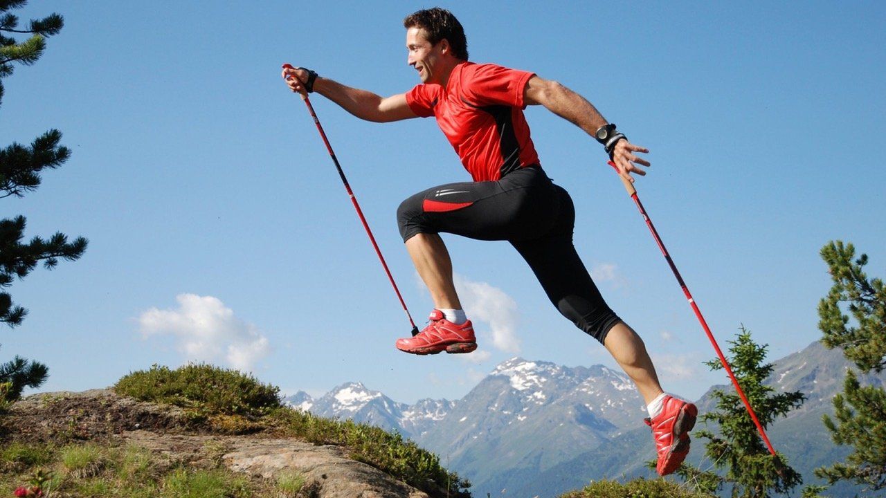 A man is jumping in the air while holding a pair of walking poles