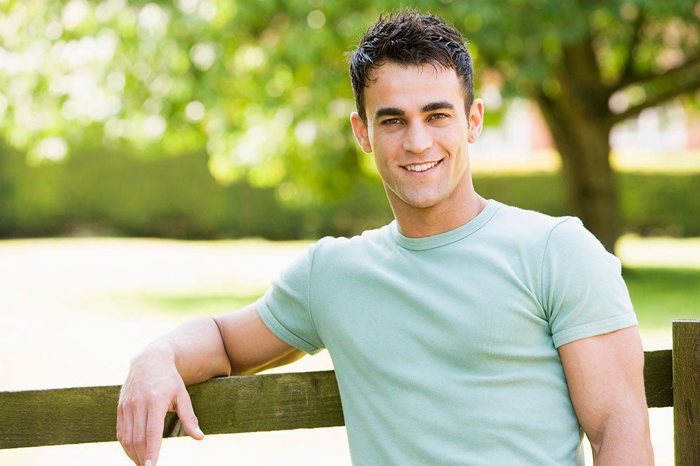 smiling young man standing by fence
