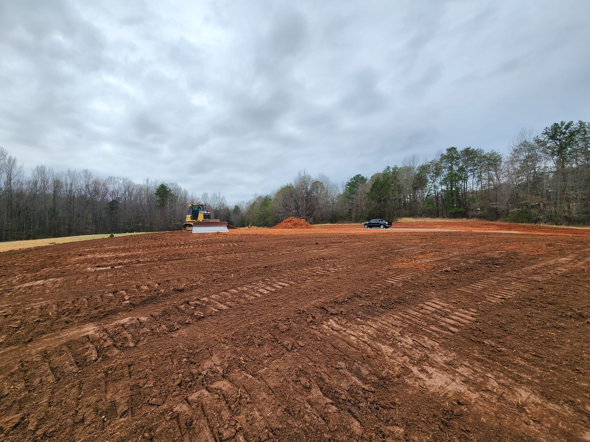 A freshly tilled field with a bulldozer and a truck; cloudy sky above.