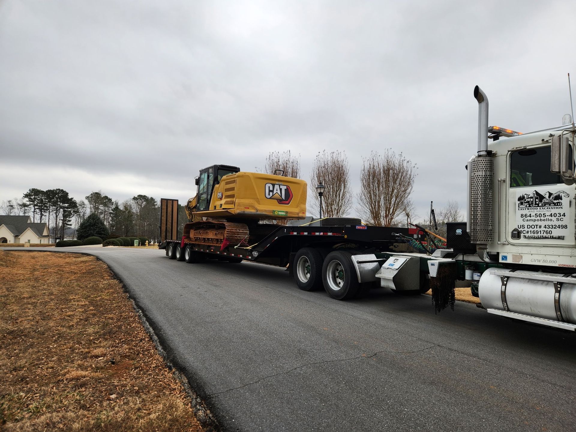 Yellow Caterpillar excavator on a flatbed trailer being hauled by a white semi-truck on a road.
