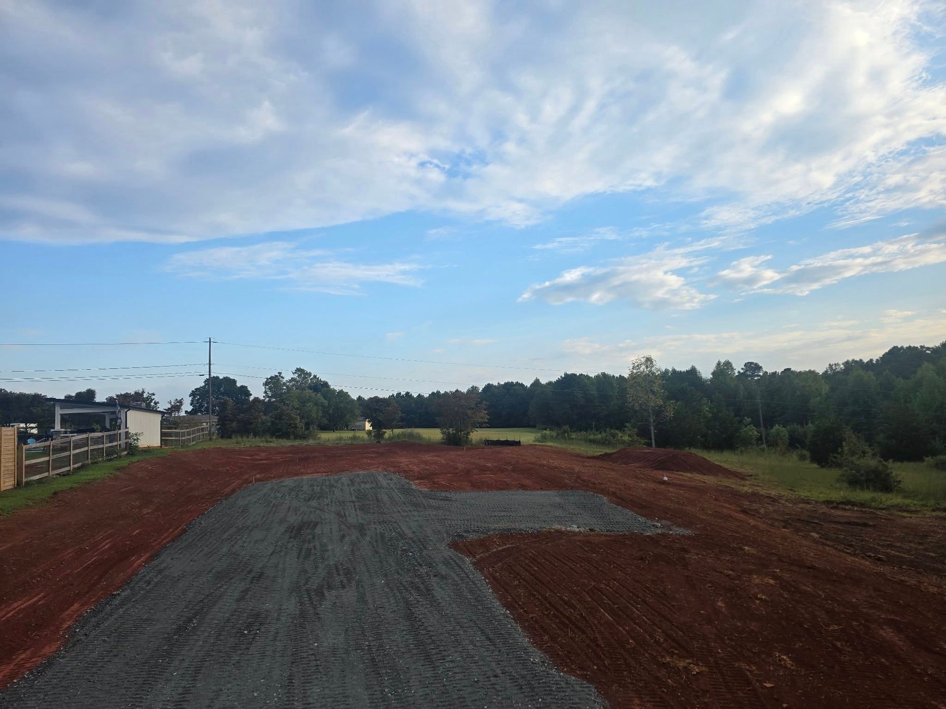 A construction site with piles of gravel and red erosion control netting under a cloudy sky.